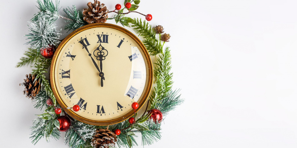 Zu sehen ist eine Uhr mit alten römischen Ziffern, die an der Wand hängt.  Sie ist eingerahmt von Tannengrün und roten Beeren 