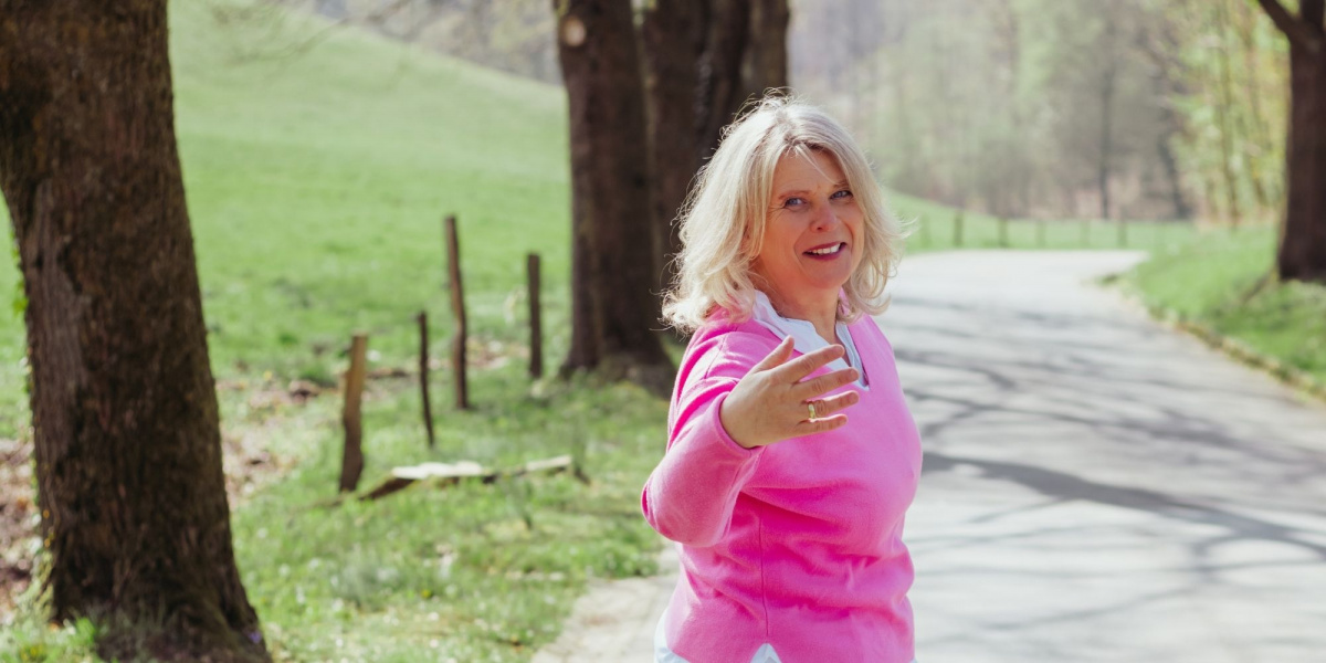 Coach für Frauen Daniela Brandl auf einem Waldweg, mit ausgestreckter Hand und offenem Lächeln.