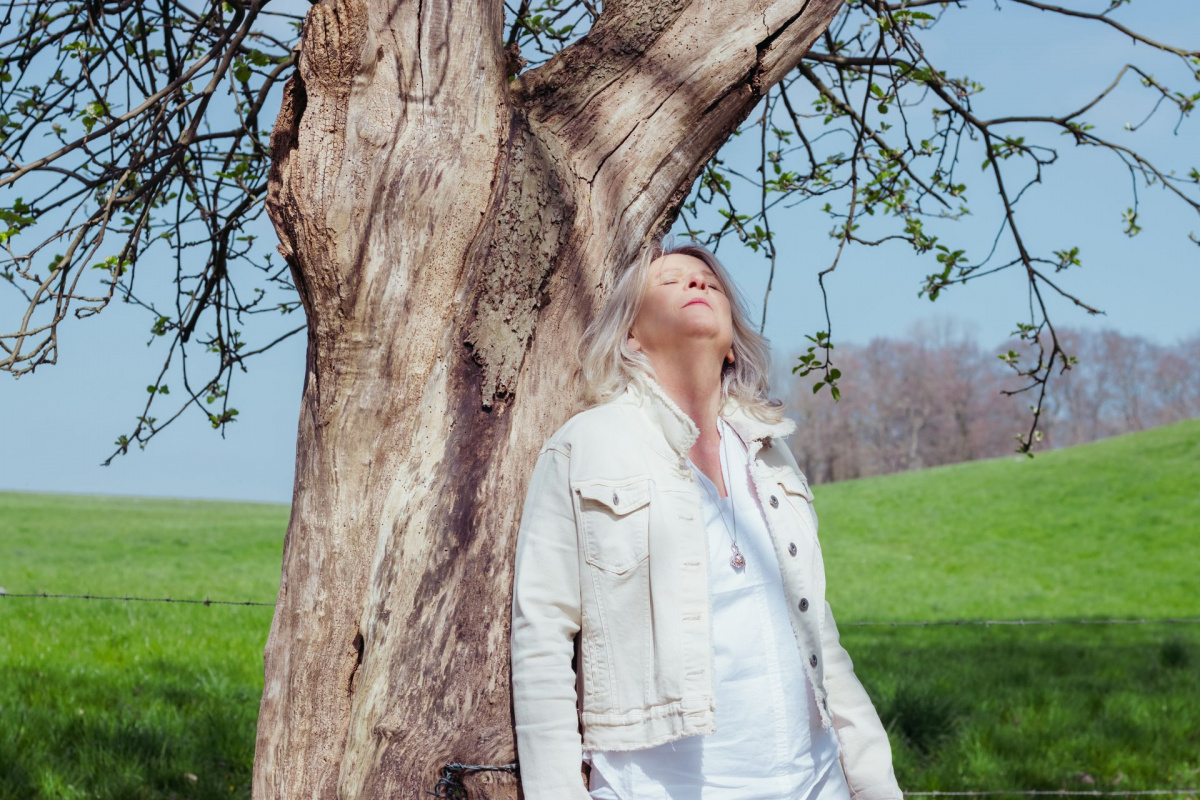 Daniela Brandl lehnt mit geschlossenen Augen an einem Baum und genießt die Sonne. Symbolbild für Leichtigkeit, Veränderung und innere Ruhe.