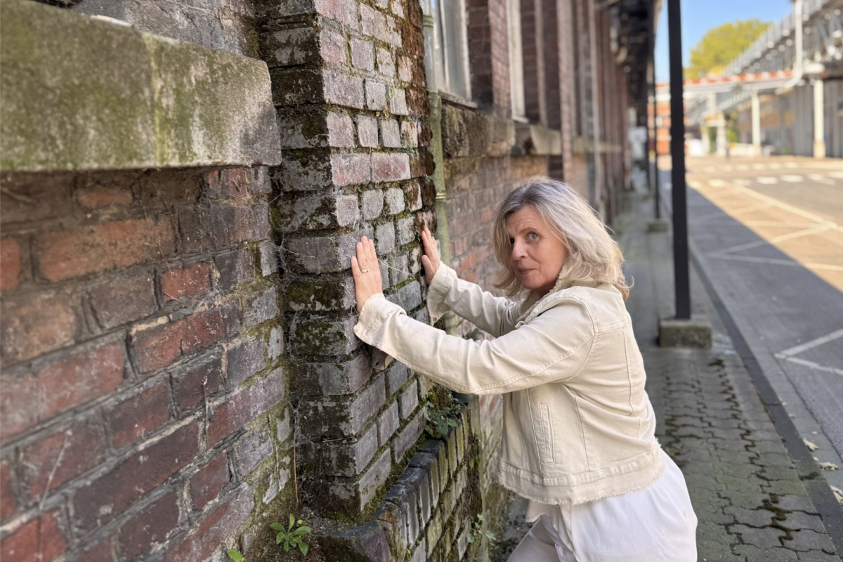 Daniela Brandl steht vor einer Mauer und versucht sie wegzuschieben