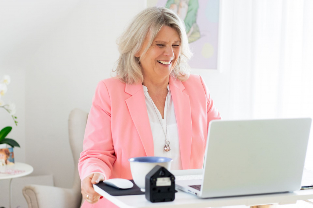 Daniela Brandl steht an einem Hochschreibtisch, vor ihr ein LapTop. Sie lacht in die Kamera.