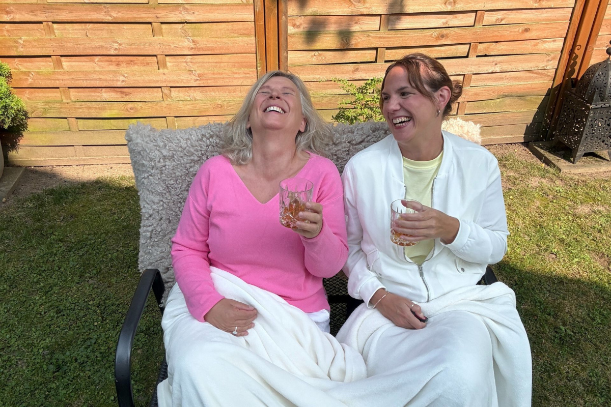 Daniela Brandl und Viola Ferrarello sitzen auf einer Bank in der Sonne und trinken Whiskey. Die Stimmung ist ausgelassen. Sie lachen und haben Freude.