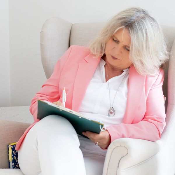 Daniela Brandl Coach sitzt in einem grauen Sessel und schreibt etwas